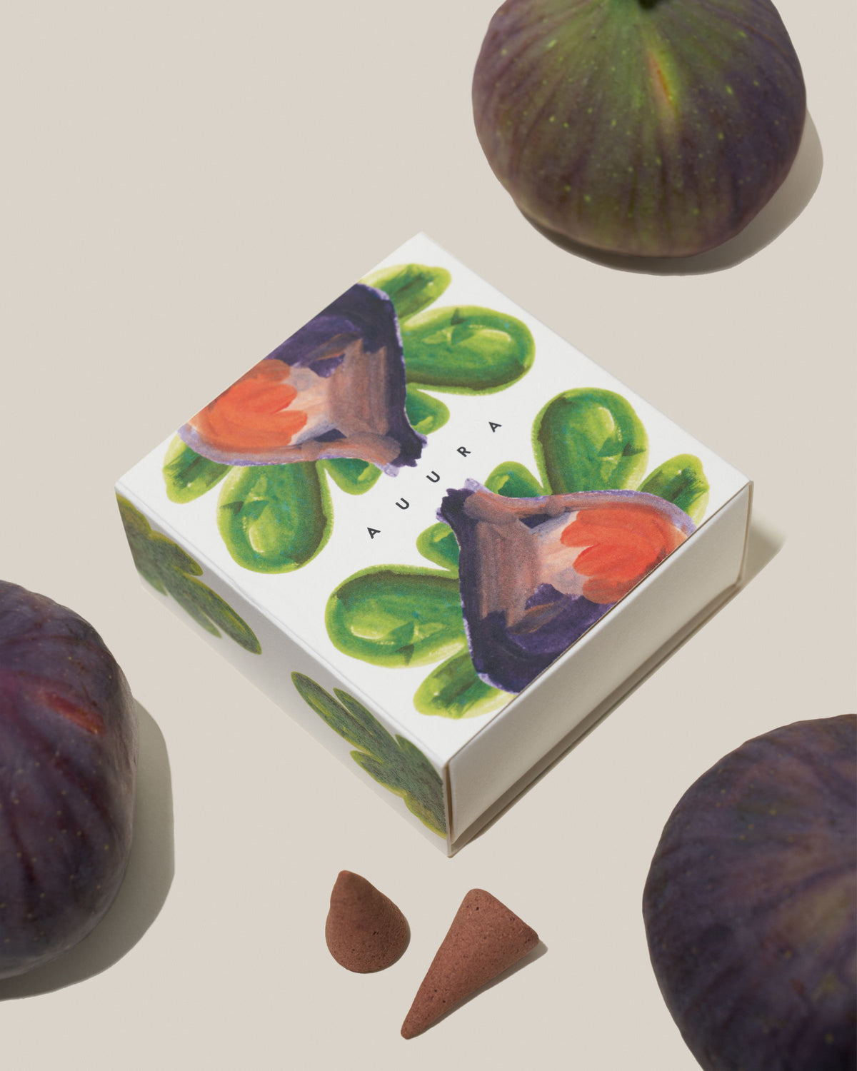 Pudełko kadzideł FIGA / KASZMERAN wśród fig i dwa stożki obok, widok z góry