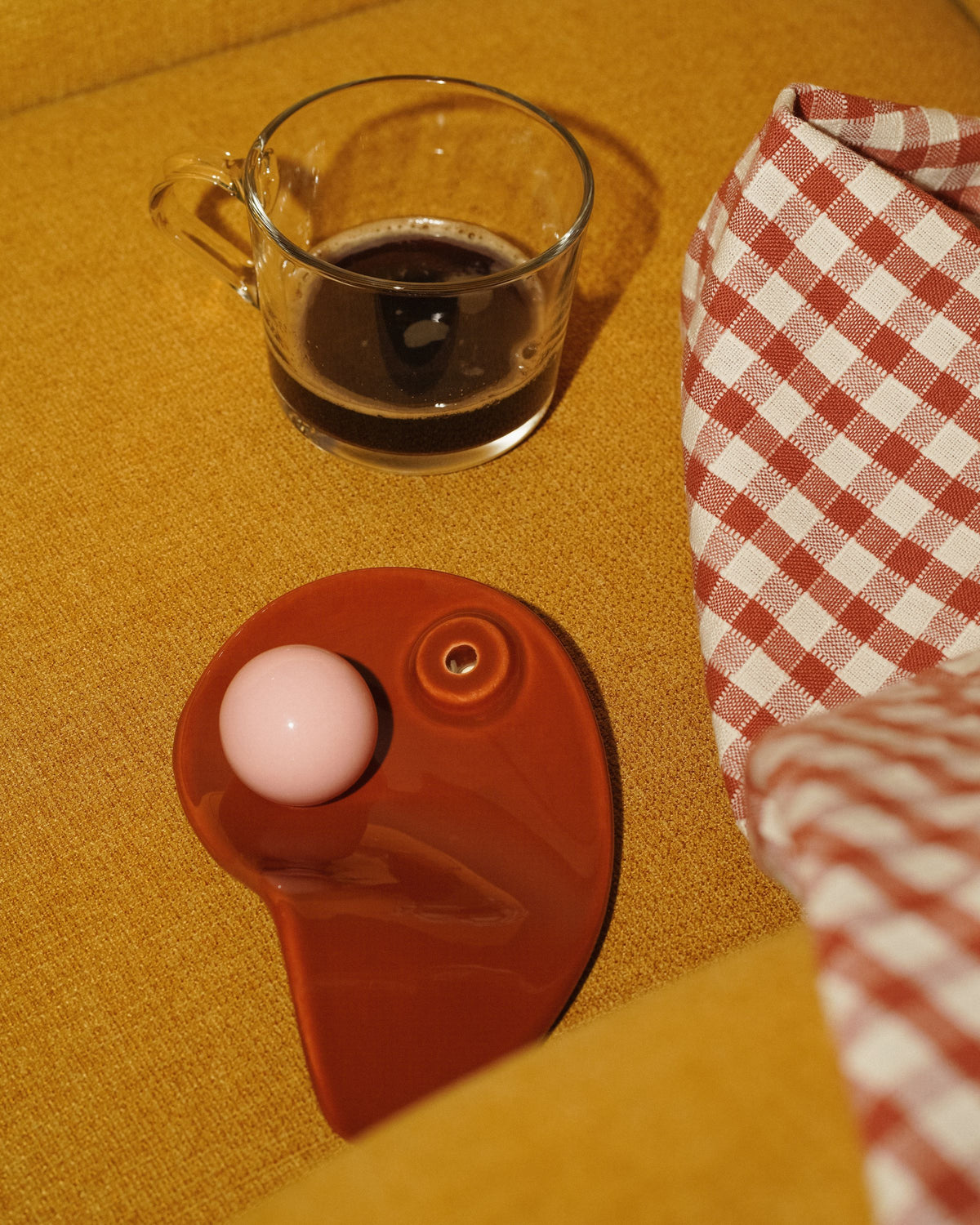 Kawa w szklance i podstawka na kadzidła AUURA CHOCO na żółtym fotelu z kraciastą tkaniną